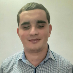 Bărbat tânăr cu păr scurt, purtând o cămașă în carouri mici, fotografiat pe un fundal simplu, deschis.